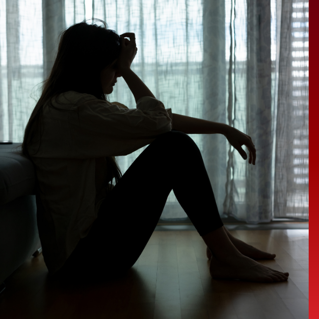 Silhouette of women sitting in front of a window with her head in her hand.